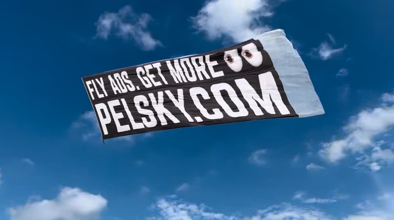 Pelican Sky banner reading Fly Ads, Get More, pelsky.com flying against a blue sky
